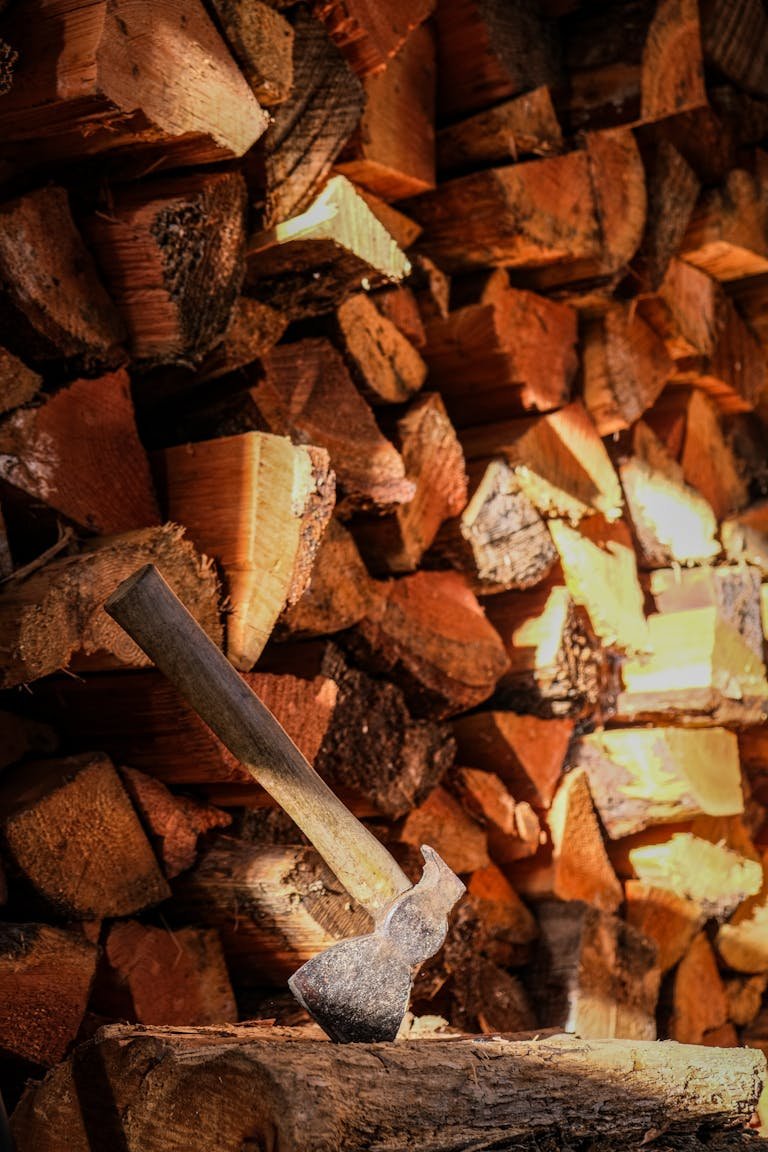 An axe embedded in chopped firewood creating a rustic and cozy autumn vibe.