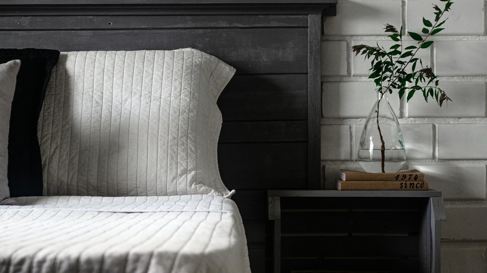 Chic rustic bedroom with cozy bedding, modern nightstand and glass vase.