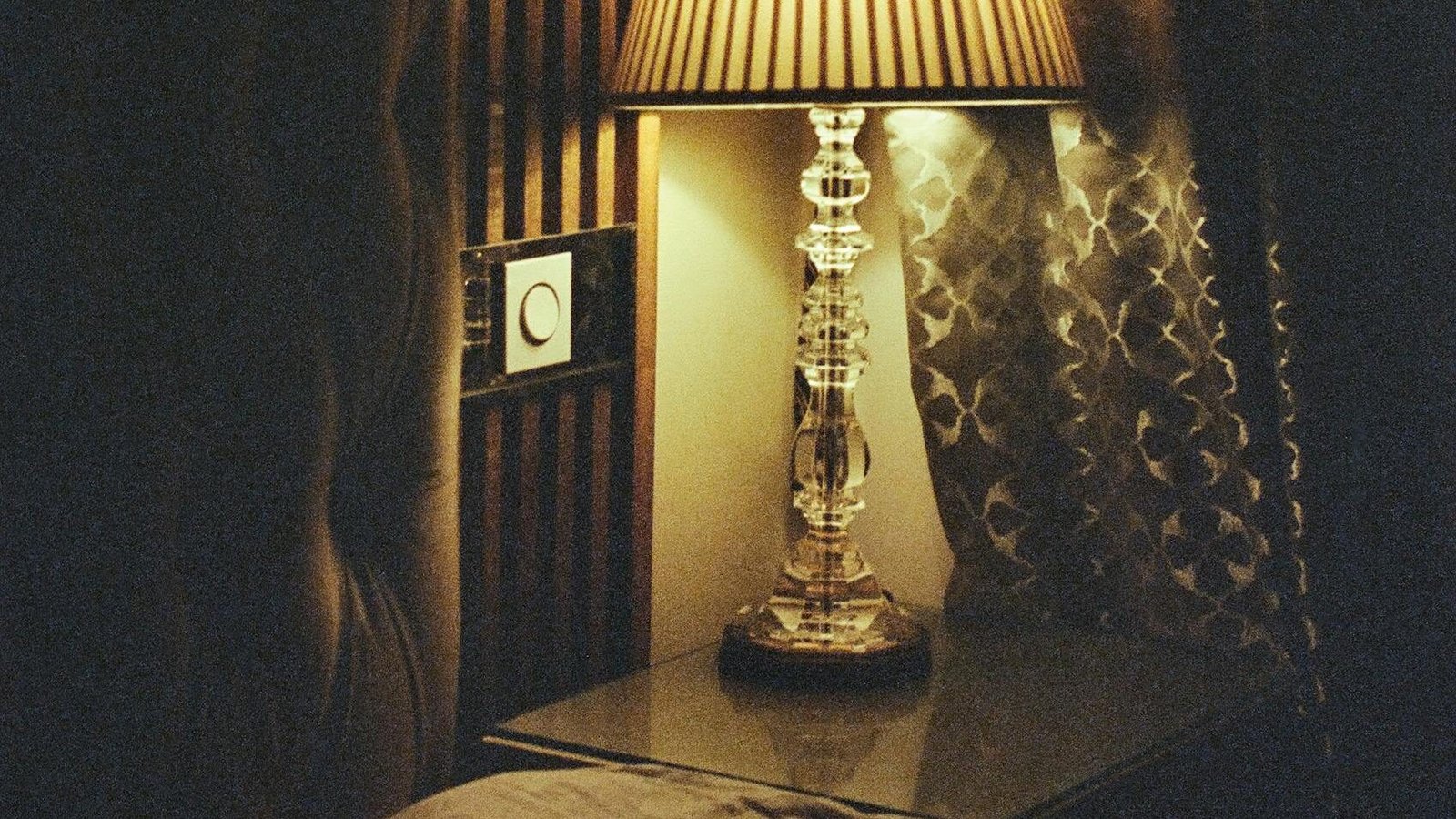 Elegant lamp on bedside table illuminating cozy bedroom corner with patterned curtains.