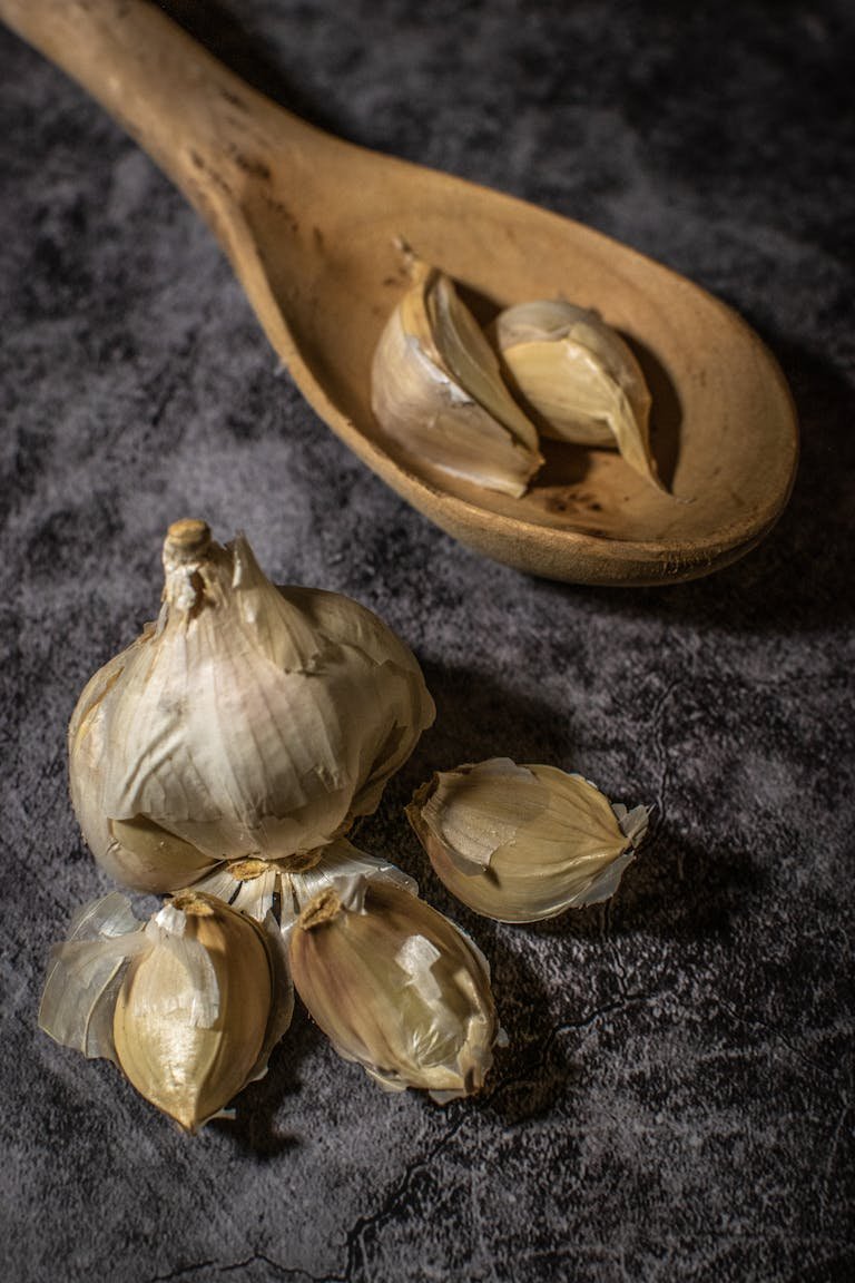 Moody still life of garlic cloves with a rustic wooden spoon on a dark background.