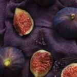Aesthetic flat lay of fresh figs on a textured purple fabric background.