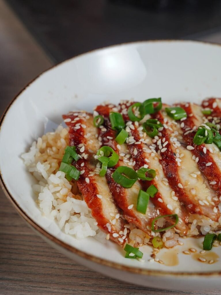 Teriyaki chicken rice bowl topped with sesame seeds and spring onions.