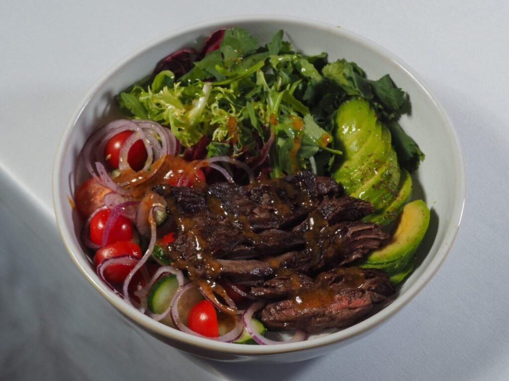 A delicious beef salad bowl with fresh vegetables and avocado, dressed with vinaigrette.